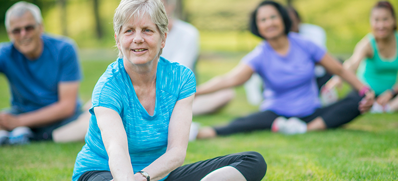 Older woman, seated, stretches during outdoor exercise class.